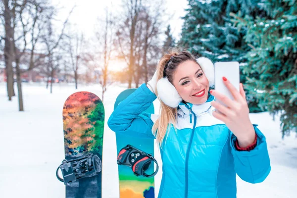 Felice ragazza prende foto telefono inverno foresta parco, sfondo albero di Natale snowboard neve, lei avendo divertimento resort. Selfie smartphone, videochiamata chat applicazione Internet. Spazio libero per il testo . — Foto Stock