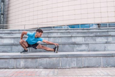 Erkek sporcu, jimnastik koşmadan önce kas esneme hareketleri. Yaz bahar şehrinde. Aktif yaşam tarzı, egzersiz, fitness temiz hava. Spor için motivasyon. Tişört şortlar spor ayakkabılar. Boş alan metni.