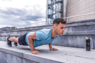 Erkek sporcu şınav çekiyor, Spring Spring City bar duruyor, göğüs kaslarını çalıştırıyor. Aktif yaşam tarzı, spor, temiz hava. Spor için motivasyon. Sulu bir şişe protein karıştırıcı.