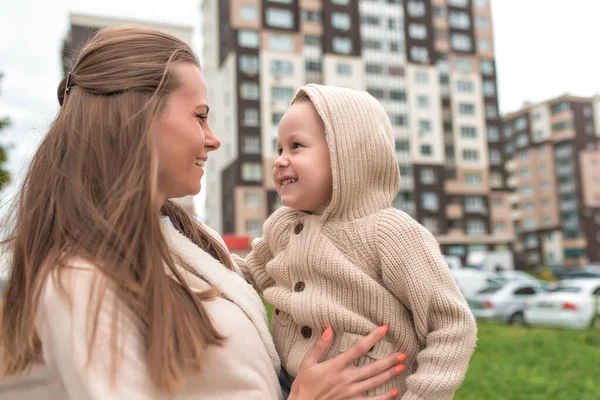 Молодая мать женщина, в ее маленьком сыне 3-5 лет, счастливая улыбка, фон высотного здания, теплая одежда бежевый свитер. Эмоции радости любви и заботы . — стоковое фото