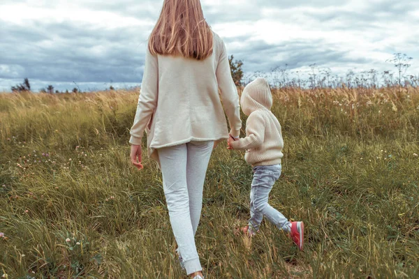 Matka žena na podzim v parku drží dětskou ruku, malý chlapec 3-5 let syn, příroda relaxovat na procházce, na jaře v terénu. Teplý oděv béžový svetr s kapucí. — Stock fotografie
