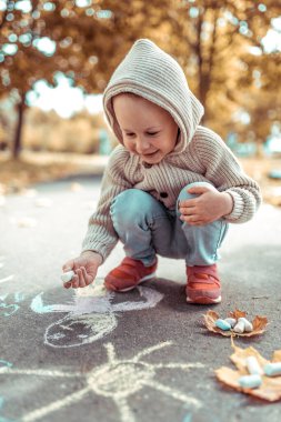 3-5 yaşlarında, renkli pastel boyalarla çizim yapan neşeli gülüşler atan, yaz sonbahar şehir parkı. Kapüşon yapraklı kalın kazak çizimi. Hafta sonu çocuk tatili kavramı.
