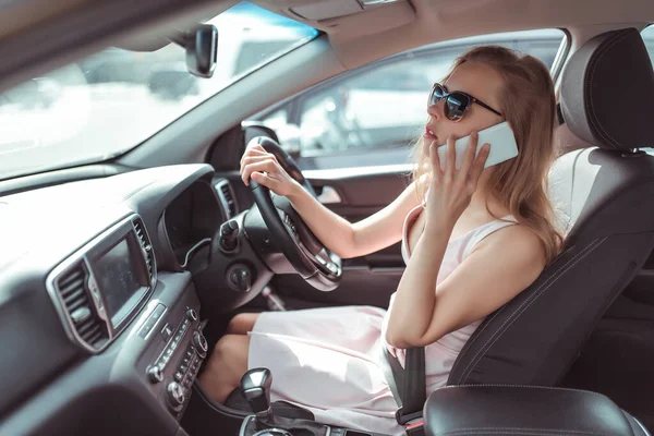 woman makes phone call, in summer city parking lot near shopping center, reversing in parking lot. Pink dress sunglasses listening to message on a cell phone.