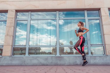 Atletik kadın sabah öğleden sonra koşu, cam pencereler arka plan, şehirde yaz eğitimi. Spor Giyim Kıyafeti Üstü. Vücut geliştirme yaşam tarzı için motivasyon. Metin için boş alan.