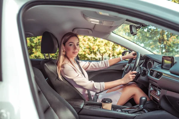 Woman wheel of car machine. In summer autumn city. Business lady driving. Background trees. Beautiful girl everyday makeup. Business class sedan. Car sharing in city car rental. — Stock Photo, Image