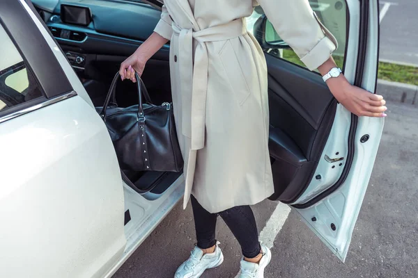 woman opens door of business class taxi car, bag in her hand after shopping, fashionable modern fashion girl, car sharing rental. In autumn summer, parking shopping center.