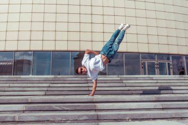 Akrobat dansçı tek kolunda durur, break dans yapar, hip-hop yapar. Summer City, arka plan binası. Aktif gençlik yaşam tarzı, genç erkek dansçı, fitness hareketi break dansçısı. Metin için boş alan.
