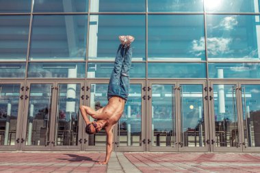 Tek kollu dansçı, akrobat aktör break dans, hip-hop. Yaz şehrinde, arka plandaki cam pencereler yaşam tarzını, genç dansçıları spor salonunun spor ayakkabılarını bulutlar. Boş alan.