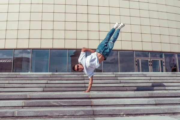Acrobat dancer stands on one arm, dancing break dance, hip-hop. Summer city, background building. Active youth lifestyle, young male dancer, fitness movement workout breakdancer. Free space for text. — Stock Photo, Image