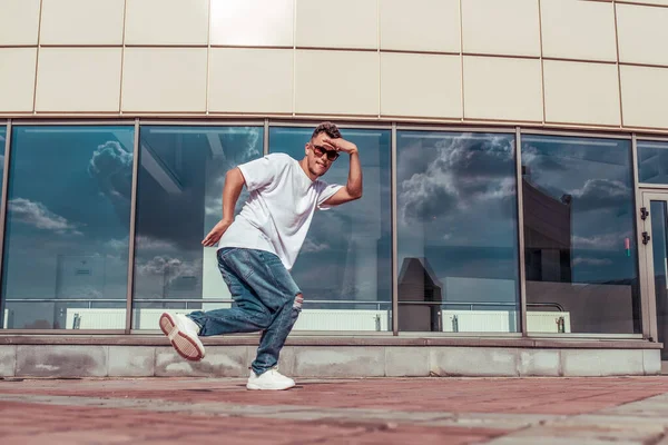 Dancer dancing break dance, hip hop. In summer city, background glass windows. Active youth lifestyle, young male dancer, fitness workout breakdancer jeans sneakers, sunglasses. Free space for text. — Stock Photo, Image