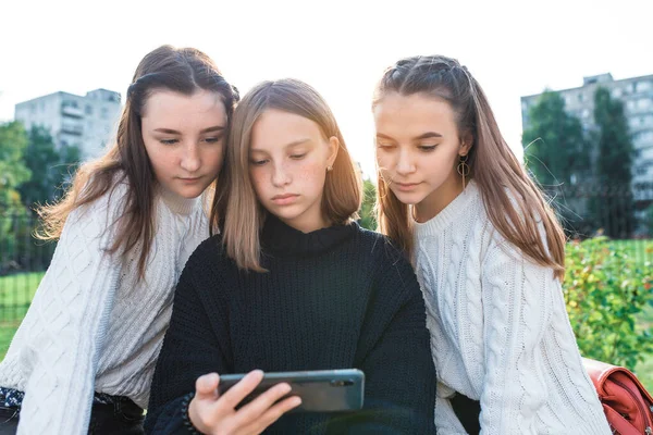 3人の女子学生のガールフレンド、スマートフォンで真剣に映画を見て。彼らはソーシャルネットワーク、インターネット上のオンラインアプリケーションを読んでいます。自然界の都市で夏に。暖かい天気の秋. — ストック写真