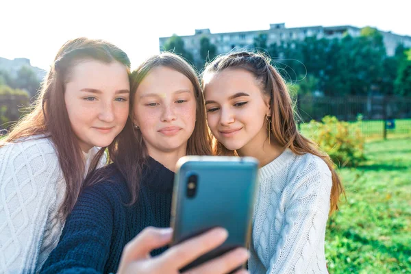Три дівчини-школярки, дивляться відео-історії соціальних мереж, фототелефони. Відео-дзвінок до онлайн-додатків про літнє місто в Інтернеті. Тепло осені.. — стокове фото