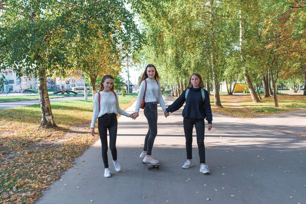 Школярки дівчата-підлітки, 3 дівчини катаються на скейтборді, розважаються влітку в парку, фонові дерева, осіннє листя, щасливі розваги, розслабляються після школи, повертаються додому . — стокове фото
