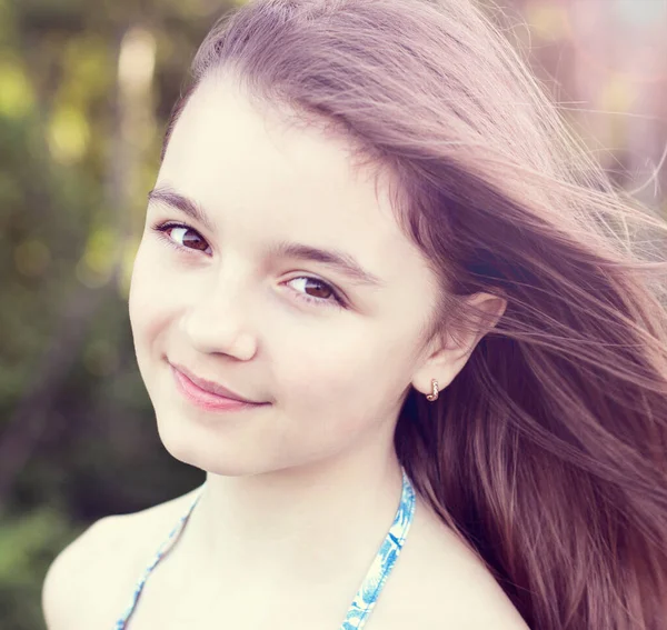 Close-up portret van kind, mooi klein tienermeisje op zoek naar bruine ogen, zomer buiten, emoties van geluk glimlach en rust. Lang haar ontwikkelt zich in de wind. — Stockfoto