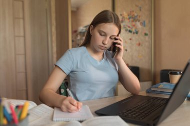 Teen girl, home lessons laptop, voice message on phone, writes task in notebook, video tutoring lessons, home education, preparing institute school. Qualification courses, video conference Internet.