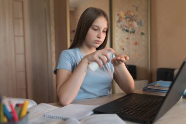 Teen girl, home lessons laptop, antiseptic spray, disinfection of hands from bacteria and viruses, video tutoring lessons, home education, preparation college school video conference on Internet.