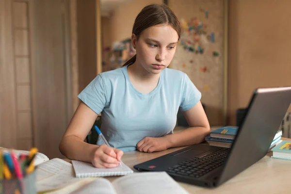 Teen girl studying home with laptop, watching videos learning, writing notebook, education home, preparing for an exam institute and school. Qualification courses, video conference on the Internet.