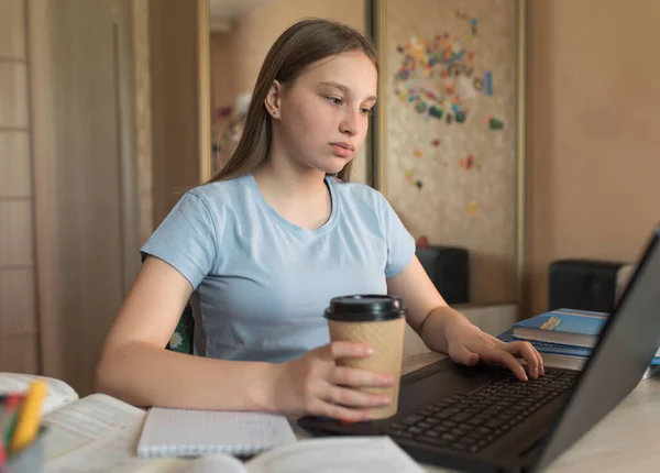 Teenagepige, hjemmeundervisning på en bærbar computer, en kop kaffe te, se videoer, læringstimer, hjemmeundervisning, forberede en eksamen på instituttet og skolen. Kvalifikationskurser, videokonference - Stock-foto