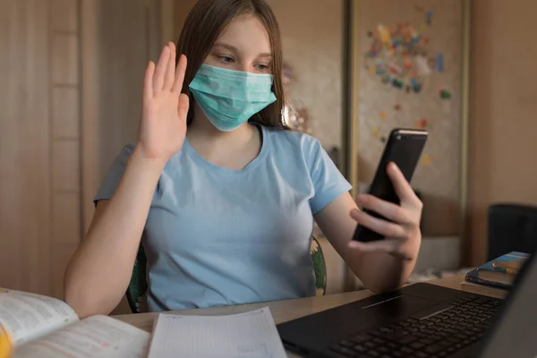 Teenager girl, in medical mask, protection viruses bacteria, video call by phone, communication with parent smartphone, education home, preparation for college school. Video conference on Internet. — Stock fotografie