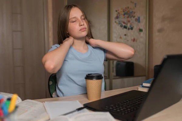 Tired girl teenager, kneading her neck from hard lesson fatigue occupation at home. Heavy preparation for school lessons and exam institute. Education video conference with teacher laptop. Stok Lukisan  