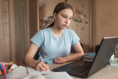 Teen girl doing homework, watching assignments exam on a laptop monitor, e-learning and online lessons, distance learning. Social networks video call, watching a teacher s lecture video on Internet.