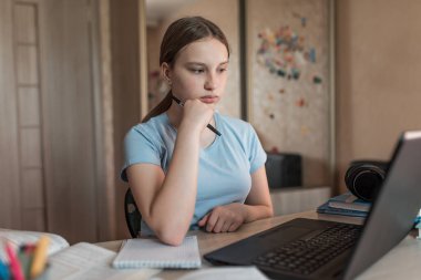 Teen girl does homework, watches videos on Internet, laptop monitor, e-education and online lessons, distance learning. Social networks video call, watching a teacher s lecture video on Internet.