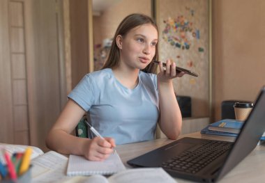 Teen girl doing homework, recording a voice message, making phone call, laptop monitor, e-education online lessons, distance learning. Social networks, watching a teacher s lecture on Internet.