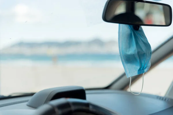 Surgical Mask hanging from the rear-view mirror of a car. Horizontal.