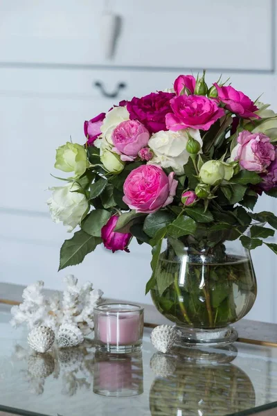 Female Interior - bouquet of fragrant pink and white English roses, shells, white coral and pink candle on the glass table