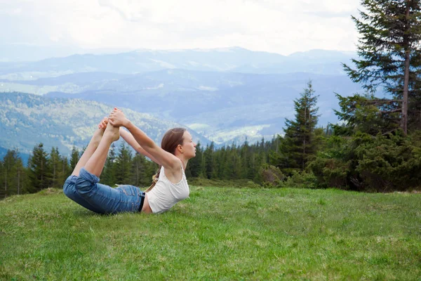 Young woman practising yoga in green mountains, dhanurasana