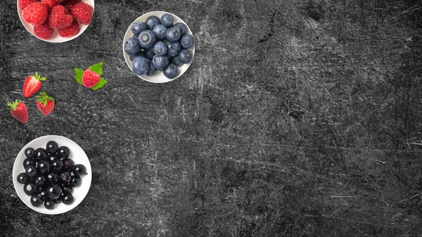 Mix of fruits on white bowls on dark background with copy space. Concept of juicy, fresh, organic and healthy. Top view of delicious and fresh berries mix on recipients.