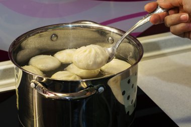 Elektrikli ocağın üzerinde metal bir tavada lezzetli khinkali pişiriyorum. Bir parça tereyağlı ve hazır vaziyette Khinkali..
