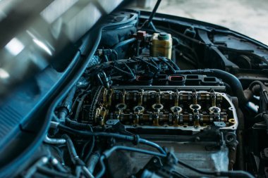 Bir araba servisinde, kaputu açık ve kısmen parçalanmış bir motoru olan bir araba durmaktadır. görünür araba motoru