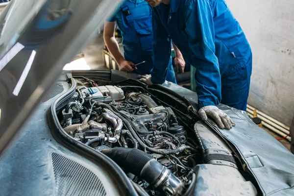 Worker in a car service inspects a car engine under the hood
