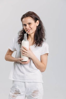 Beyaz bir stüdyoda beyaz elbiseli, genç, güzel esmer bir kız elinde bir bardak süt, pipetten içiyor..