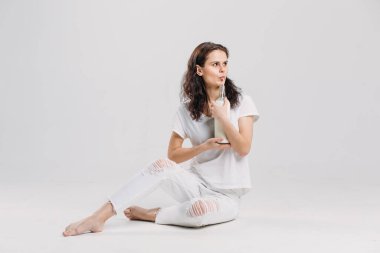 Beyaz bir stüdyoda beyaz elbiseli, genç, güzel esmer bir kız elinde bir bardak süt, pipetten içiyor..