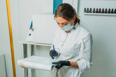 Aydınlık oda tıbbi bir laboratuara benziyor. Odada kuartlama ve işleme aletleri için bir cihaz var. Çerçevede, maske takan ve tıbbi elbise giyen bir kız doktora çok benziyor. İnceleme yapıyor ve bir günlüğe yazıyor.