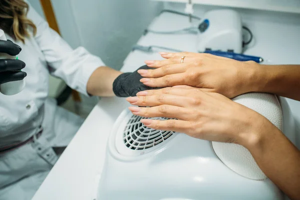 Nail salon, the master does nail care for the client. a master in a dressing gown and a mask, in the frame of the hand, moments of action with the client's nails