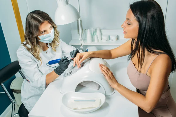 Nail salon, the master does nail care for the client. a master in a dressing gown and a mask, in the frame of the hand, moments of action with the client's nails