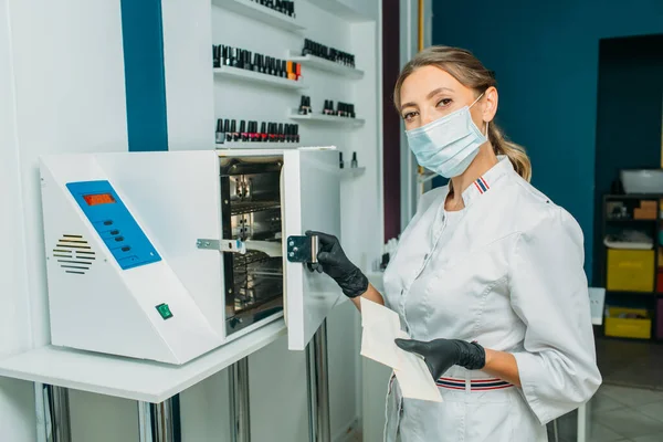 the bright room looks like a medical laboratory, there is an apparatus for quartzing and processing objects in the room. in the frame, a girl in a mask and a medical gown looks very much like a doctor makes an examination and writes in a journal