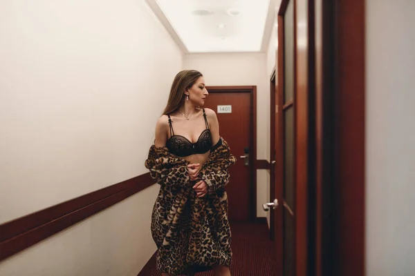 客室の間の廊下には ホテルだけで夜の若い美しい女の子が歩いています 黒い下着と毛皮のコートを着ていて — ストック写真