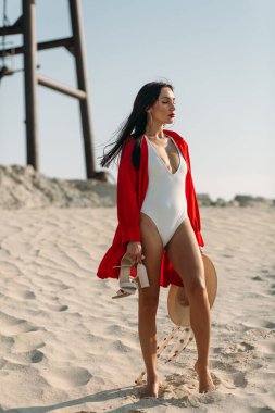 Güzel vücutlu genç bir kız, sadece beyaz kum ve mavi gökyüzü etrafında, ve üzerinde beyaz bir mayo ve güzel aksesuarlar