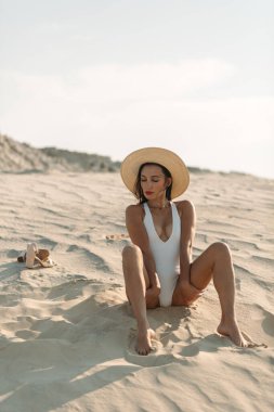 Güzel vücutlu genç bir kız, sadece beyaz kum ve mavi gökyüzü etrafında, ve üzerinde beyaz bir mayo ve güzel aksesuarlar