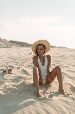 Güzel vücutlu genç bir kız, sadece beyaz kum ve mavi gökyüzü etrafında, ve üzerinde beyaz bir mayo ve güzel aksesuarlar