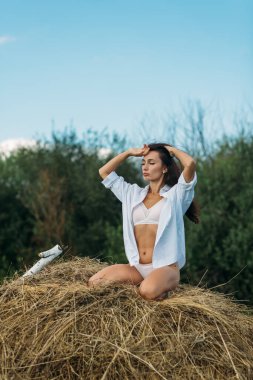 Uzun siyah saçlı ve güzel vücutlu genç bir kız, açık renk iç çamaşırlı ve gömlekli bir kız, tarlada yürüyor, yaz, güneş, gökyüzü, gün batımı yeşili tarlalar,.