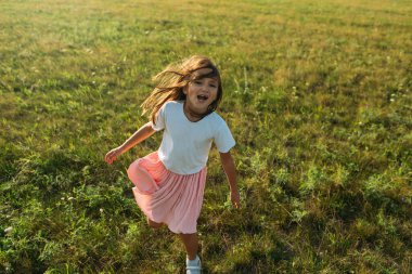 Saçları açık ve yanaklarında güneşli bir parıltıyla yedi yaşlarında küçük bir kız, yaz aylarında ailesiyle birlikte tarlada yürüyor. Yeşillik, güneş, gökyüzü, çimenler. Koşuyor, tartıyor ve ebeveynlerini ellerinden tutuyor.