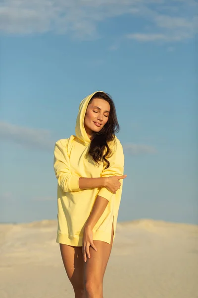 A young beautiful girl with a good figure, around only white sand and blue sky, she is wearing a yellow sweater