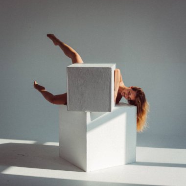 Plastik figürlü genç bir kız, stüdyoda beyaz küpleri yalıyor, plastikleri gevşetiyor, pencereden gelen güneş ışığı onun üzerinde parlıyor..