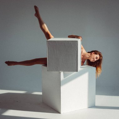 Plastik figürlü genç bir kız, stüdyoda beyaz küpleri yalıyor, plastikleri gevşetiyor, pencereden gelen güneş ışığı onun üzerinde parlıyor..