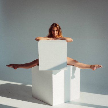 Plastik figürlü genç bir kız, stüdyoda beyaz küpleri yalıyor, plastikleri gevşetiyor, pencereden gelen güneş ışığı onun üzerinde parlıyor..